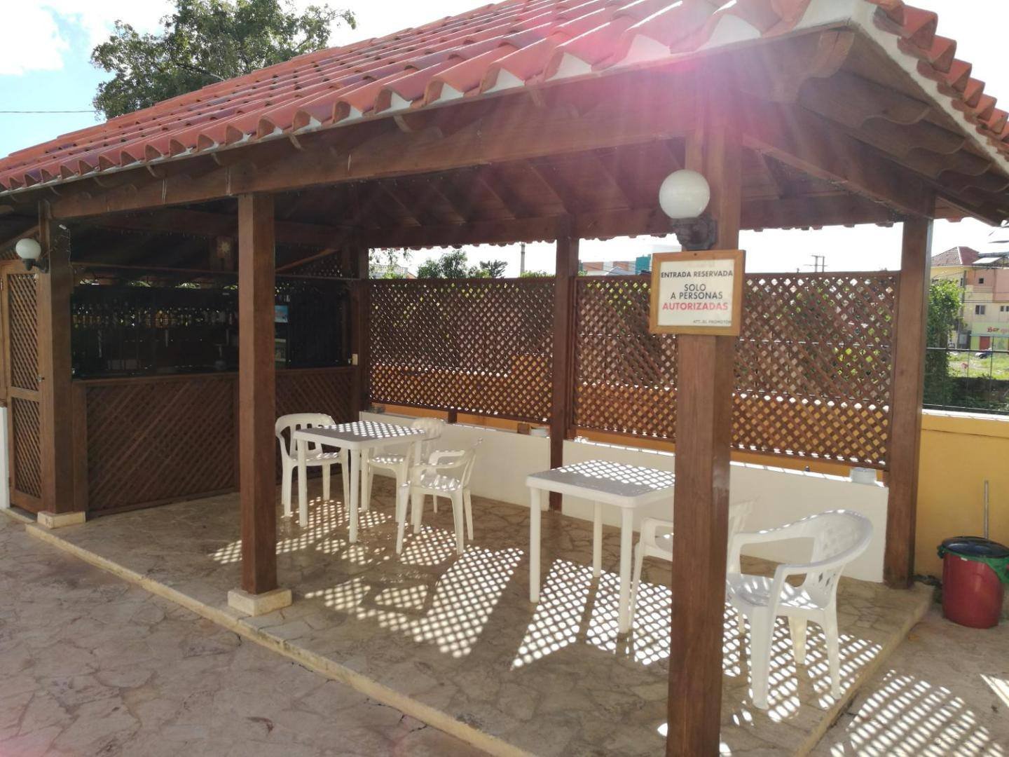 Covered wooden terrace with white plastic tables and chairs next to the pool