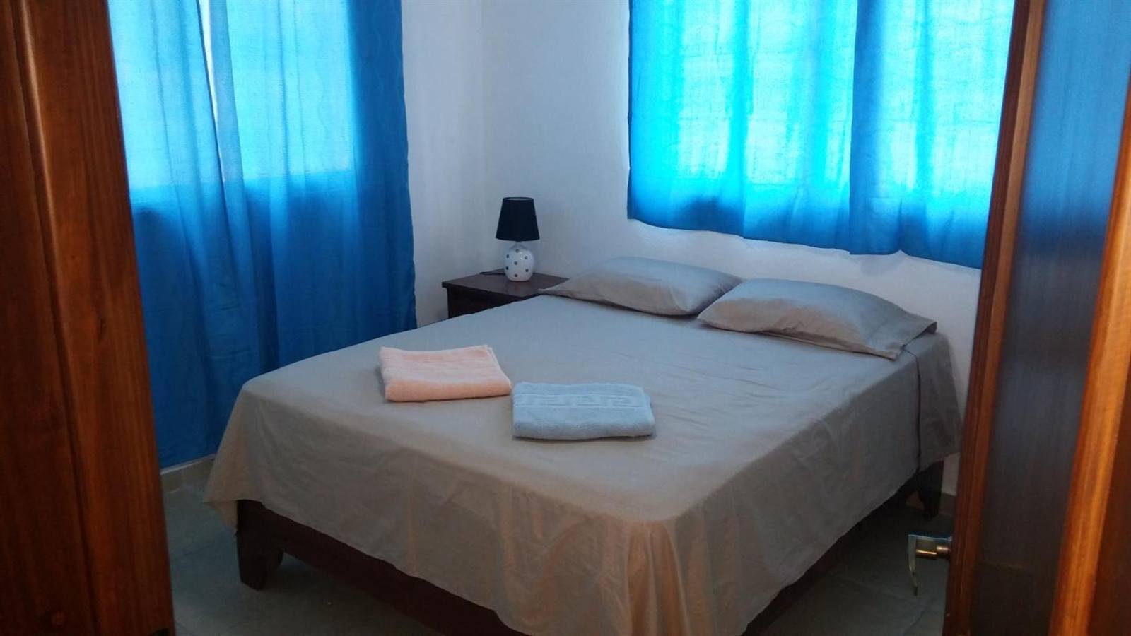 Bedroom with a double bed, blue curtains and a bedside lamp